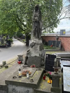 Stare nagrobki na cmentarzu z postacią w długim płaszczu i zniszczoną powierzchnią pomnika
