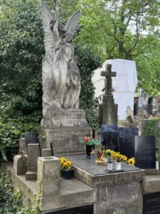 Stare nagrobki na cmentarzu z dużą rzeźbą anioła trzymającego krzyż nad modlącą się kobietą