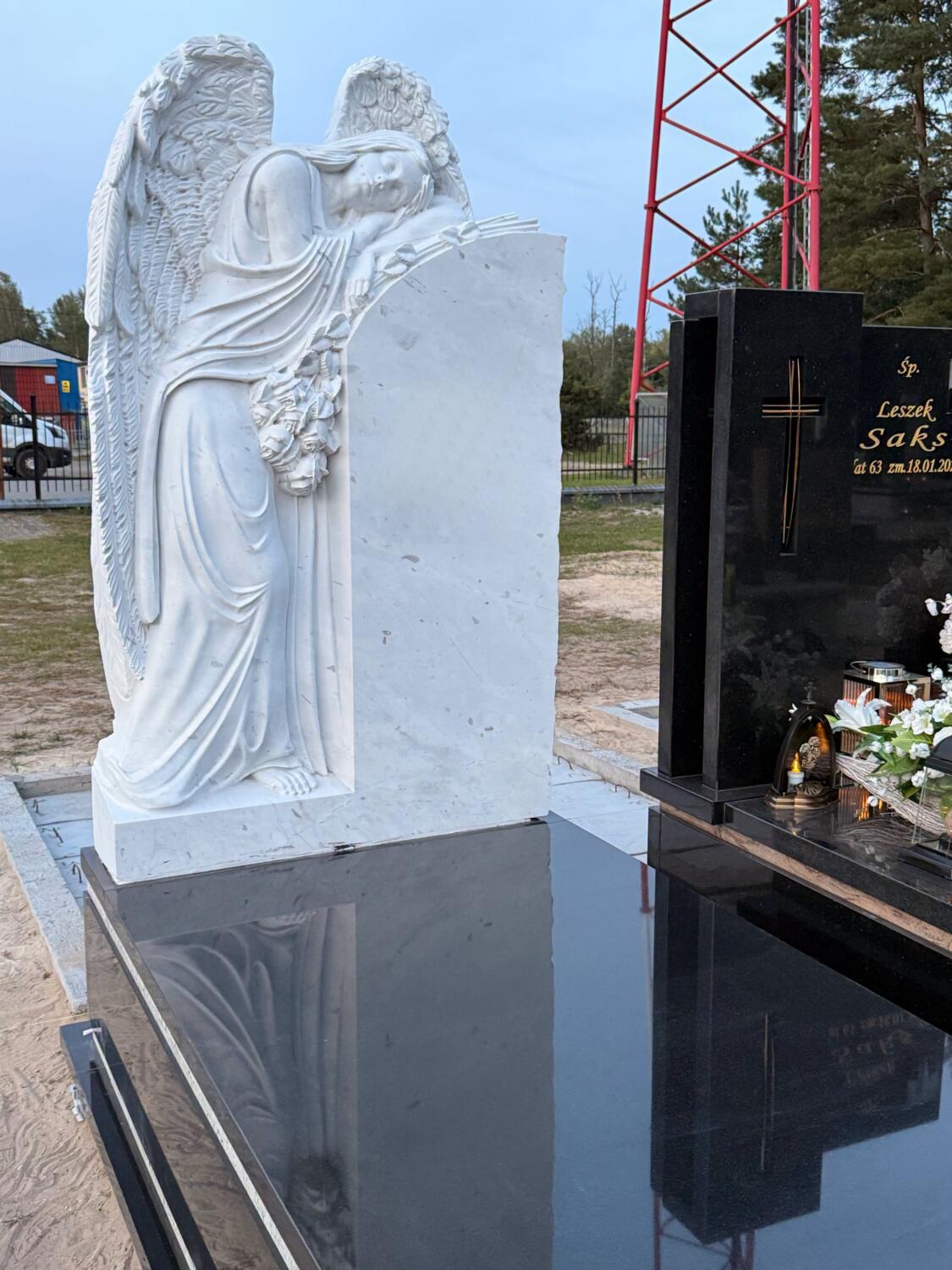 Marmurowy anioł ze skrzydłami i dłońmi przy jasnej tablicy, widok bardziej od przodu na ciemnej płycie — GRAAL
