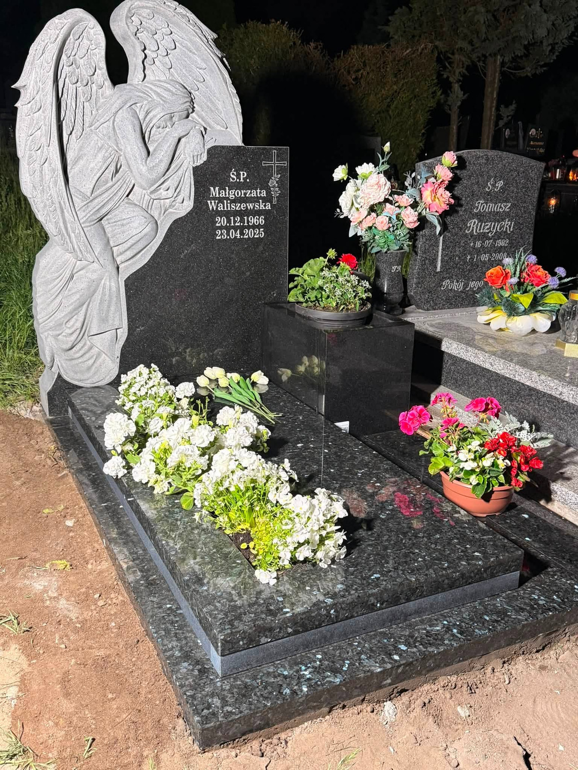 Podłużne białe kwiaty na ciemnej płycie i mniejsza dekoracja w niskiej misie po prawej