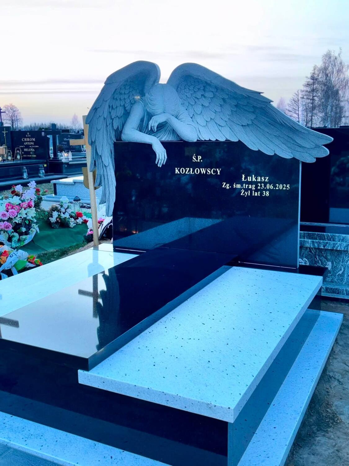 Nagrobek podwójny z aniołem, szeroką ciemną stelą i podwyższoną środkową płytą między jasnymi bokami