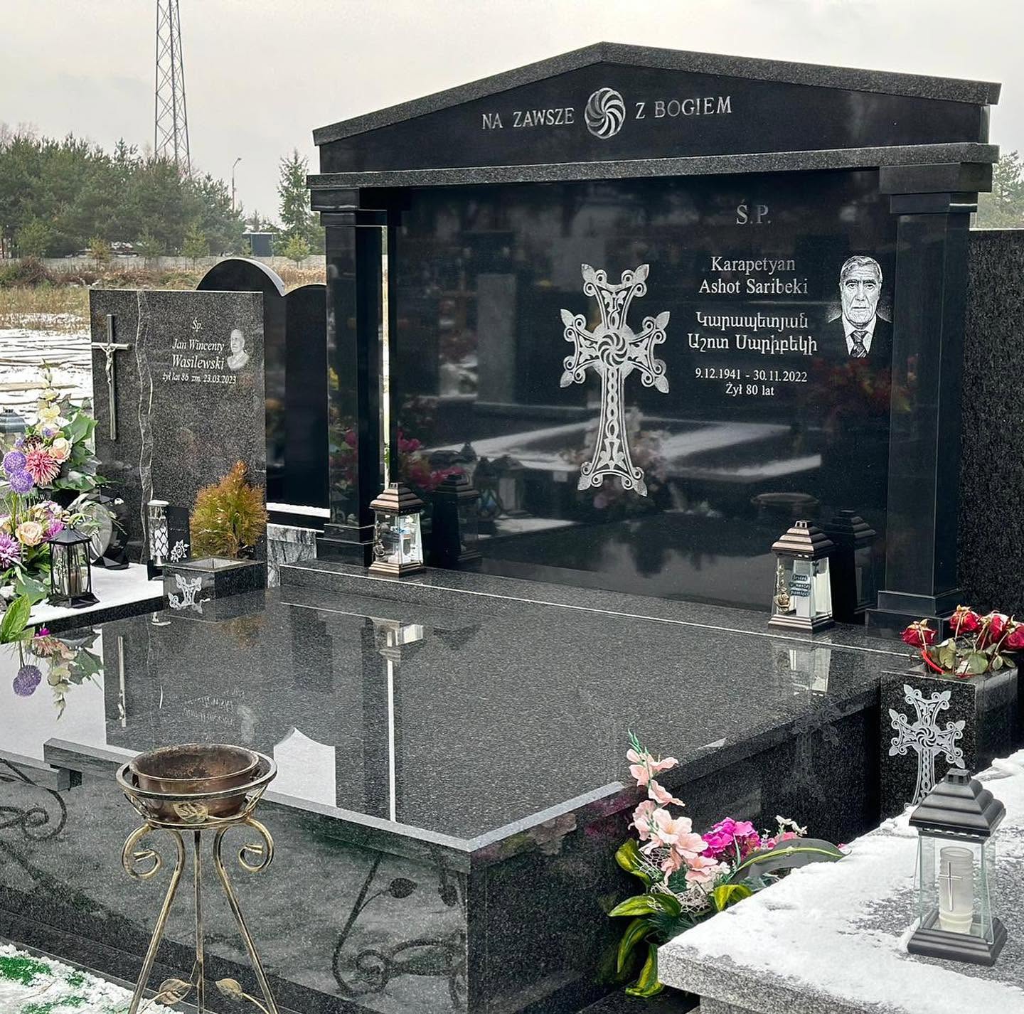 Nagrobek rodzinny z szeroką ciemną tablicą, ozdobnym grawerem krzyża i klasycznym zwieńczeniem