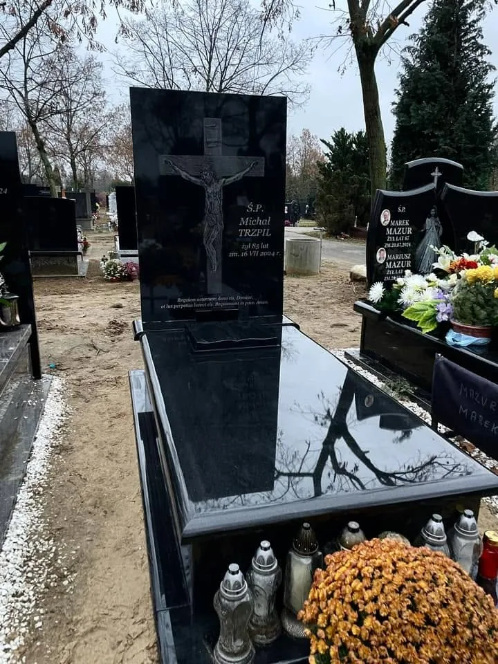 Kwiaty i znicze przed ciemną płytą nagrobną — fotografia GRAAL