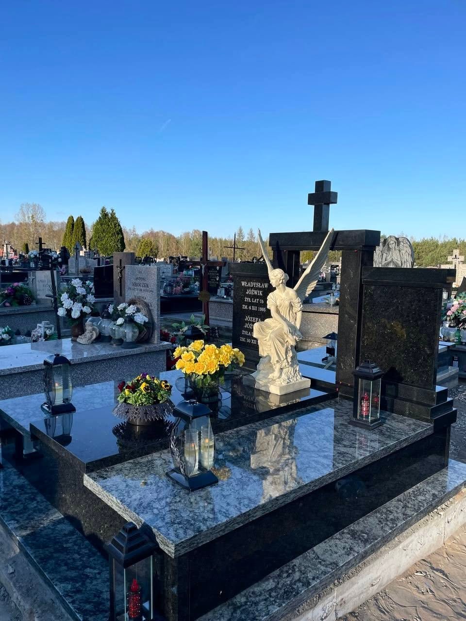 Nagrobek podwójny z dwiema bocznymi tablicami, wysokim krzyżem i jasną rzeźbą anioła pośrodku — realizacja GRAAL