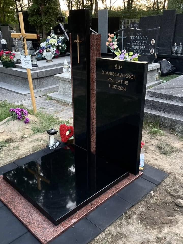 Ukośny widok nagrobka urnowego GRAAL z napisem Stanisław Król, ciemnym wysokim krzyżem i czerwonymi pasami