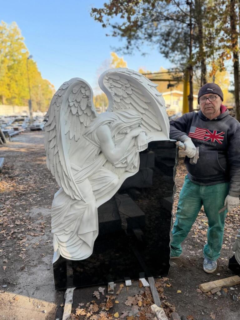 Biała figura anioła z przestrzennymi skrzydłami i fałdami szaty przy ciemnym elemencie pomnika — fotografia GRAAL
