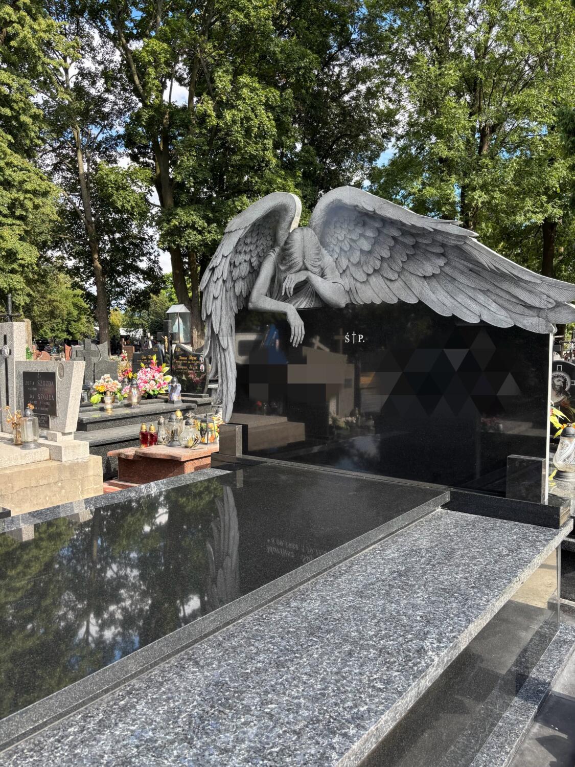 Szara rzeźba anioła z szeroko rozłożonym skrzydłem przy ciemnej tablicy w dokumentalnej fotografii GRAAL